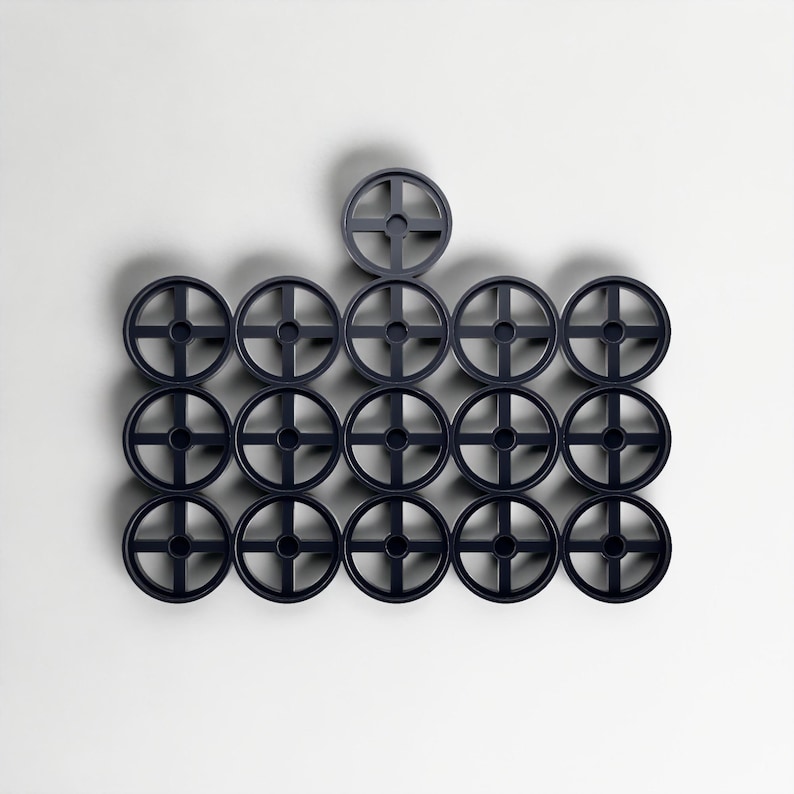May include: A collection of dark grey circular objects, each featuring a cross-shaped design at the centre. They are arranged in a grid formation against a white backdrop, forming a geometric pattern.
