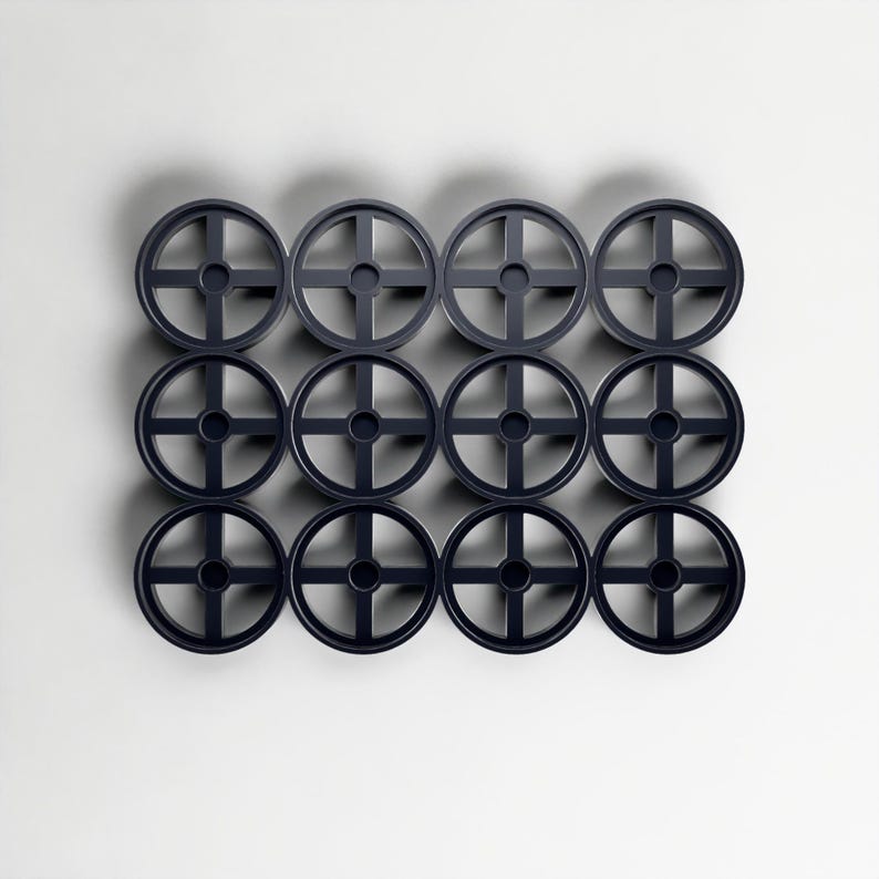 May include: A grid of twelve dark grey circular objects, each with a cross-shaped centre and a wheel-like design. The objects are arranged in a neat pattern against a plain white background. Each object has a diameter of approximately 10 cm.