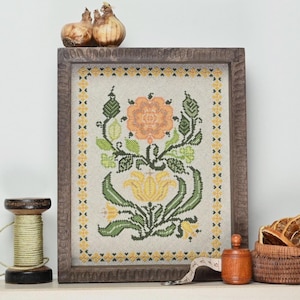 May include: A framed cross-stitch floral design featuring an orange rose and yellow tulip. The embroidery is set against a neutral background and framed in a dark wood. Decorative elements include a wooden spool, a small basket, and bulbs.