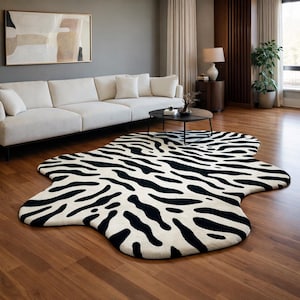 May include: A black and white zebra-print area rug with an irregular shape. The rug is placed on a hardwood floor in a living room setting, with a white sofa and coffee table visible in the background. The rug's design adds a bold statement to the room's decor.