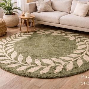 May include: A circular, olive green rug featuring a cream laurel wreath pattern. The rug, made of soft material, sits on a wooden floor. The rug's diameter is approximately 213 cm.