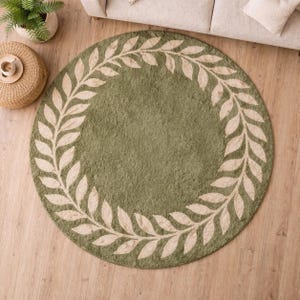 May include: A circular olive green rug featuring a cream-coloured leaf border design. The rug is made from a soft, plush material, suitable for living rooms or bedrooms. The rug's diameter is approximately 152 cm.