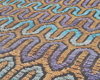 May include: A textile surface featuring a repeating pattern of wavy, interconnected lines in shades of light blue, lavender, and tan. The material has a textured, tufted appearance with a consistent pile height across the entire fabric surface.