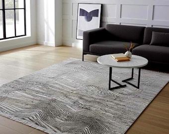 May include: A rectangular area rug featuring a monochromatic pattern of dark grey and white zigzag lines. The rug has a textured appearance with short fringe detailing along the edges, positioned on a light-coloured wooden floor in a room.