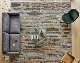 May include: A rectangular area rug featuring a light grey base with a repeating pattern of horizontal, oval-shaped motifs in shades of olive green, rust orange, and mustard yellow. The rug has a textured weave and short fringe on both ends.