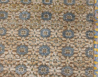 May include: A woven textile featuring a repeating geometric pattern of blue circular motifs set against a tan and beige background. The design includes intricate floral-like shapes and a border on the right side with yellow and blue accents.