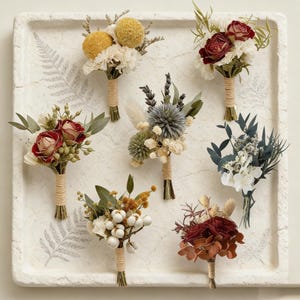 Pode incluir: Uma variedade de sete pequenos buqu&ecirc;s de flores secas, cada um com um arranjo &uacute;nico de flores e folhagens. Os buqu&ecirc;s s&atilde;o amarrados com barbante e repousam em uma bandeja branca texturizada. As cores incluem vermelho, amarelo, verde e branco.