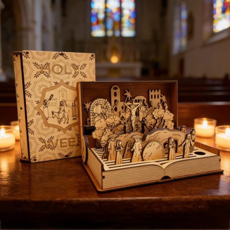 May include: A wooden laser-cut book with an open diorama depicting a religious scene. The book cover is tan with decorative patterns and the word "HOLY" and "AVEE" printed on it. The diorama features figures, trees, and architectural elements.