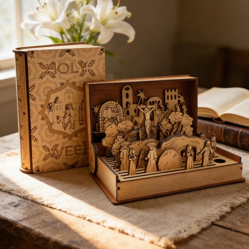 K&ouml;nnte beinhalten: Holzbox in Buchform mit lasergeschnittener religi&ouml;ser Szene. Die offene Box zeigt eine detaillierte Darstellung eines biblischen Ereignisses. Auf dem geschlossenen Buch stehen die Worte "HOLY" und "WEEK". Wei&szlig;e Lilien sind im Hintergrund.