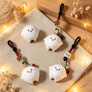 May include: Four white wooden figurines with smiling faces and small black eyes. Each figure has a textured surface and is attached to a brown cord with decorative beads. One cord has the characters "Peace" on it.