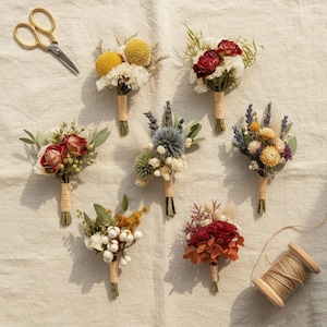 Pode incluir: Vista a&eacute;rea de v&aacute;rios pequenos buqu&ecirc;s de flores secas em v&aacute;rias cores e texturas, cada um amarrado com barbante. Tamb&eacute;m est&atilde;o presentes uma tesoura dourada e um carretel de barbante, sugerindo um tema de artesanato ou arranjo floral.