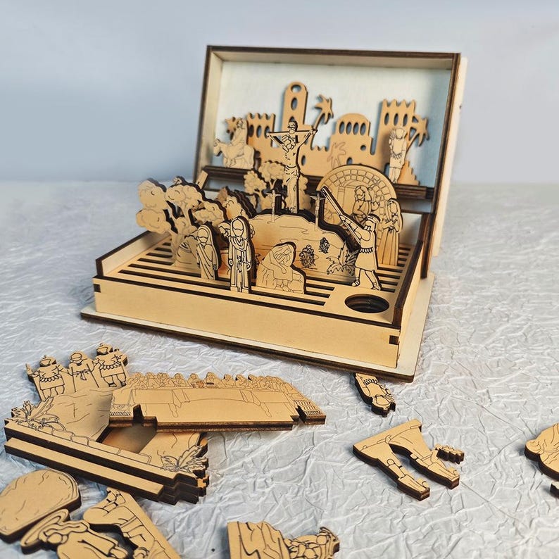 K&ouml;nnte beinhalten: Ein Diorama aus Holz mit Laserschnitt, das eine religi&ouml;se Szene darstellt, mit Figuren und Strukturen. Die Szene umfasst eine Kreuzigung, Figuren in Gew&auml;ndern und architektonische Elemente. Zus&auml;tzliche Holzst&uuml;cke sind verstreut.