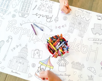 Puede incluir: Una hoja para colorear blanca con temática parisina, con ilustraciones de monumentos como la Torre Eiffel y el Moulin Rouge. Las palabras "Happy Birthday" se muestran de forma destacada. Un cubo rojo lleno de crayones está cerca.