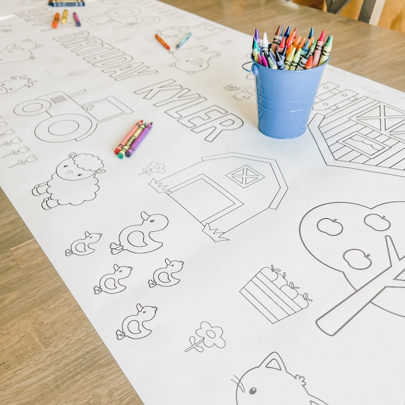 May include: A white colouring tablecloth with a farm theme. The tablecloth features a tractor, a barn, a sheep, ducks, an apple tree, a flower, and a cat. The text "Happy Birthday Kyler" is printed on the tablecloth. A bucket of crayons is on the table.