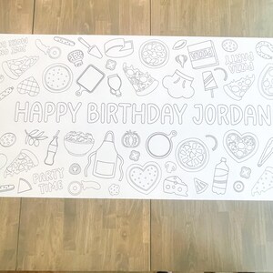 White paper table runner with a black outline design of pizza-themed illustrations. The words "HAPPY BIRTHDAY JORDAN" are prominently displayed. Includes pizza slices, pizza boxes, and other party-related graphics.