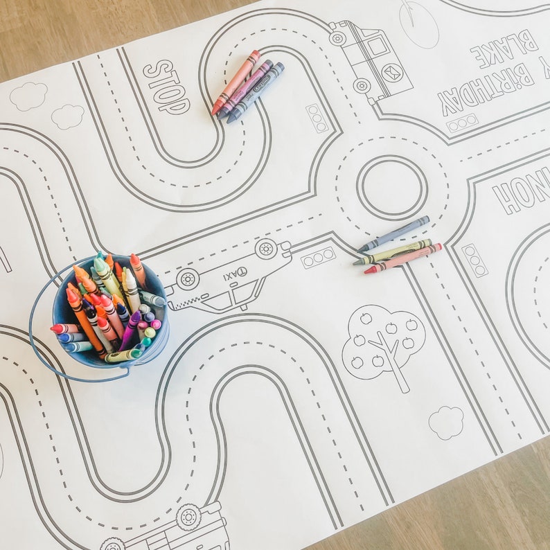 May include: A white colouring mat with a road map design, featuring cars, a stop sign, and a tree. The mat is labelled "Happy Birthday Blake" and includes a bucket of crayons.