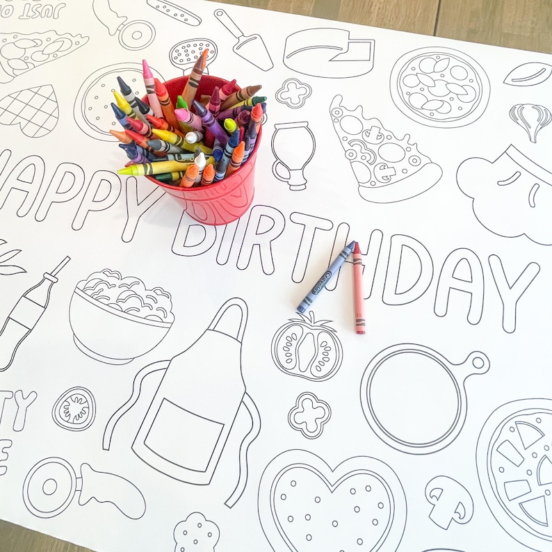 A white paper tablecloth with black outlines of pizza-themed illustrations and the words "HAPPY BIRTHDAY." A red bucket filled with colorful crayons sits on the table, along with two crayons.