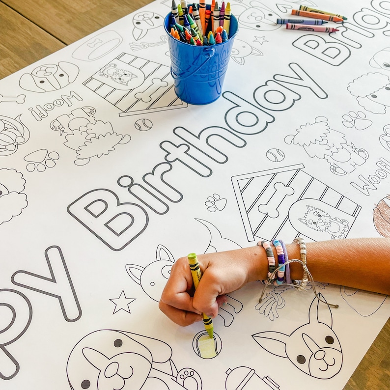 Pu&ograve; includere: Un foglio da colorare bianco con un tema di compleanno di cane. Il foglio presenta una variet&agrave; di illustrazioni di cani, tra cui una cuccia, ossa e impronte di zampe. Il testo "Buon compleanno" &egrave; scritto in cima al foglio. Una mano di bambino sta colorando il foglio con un pastello verde.