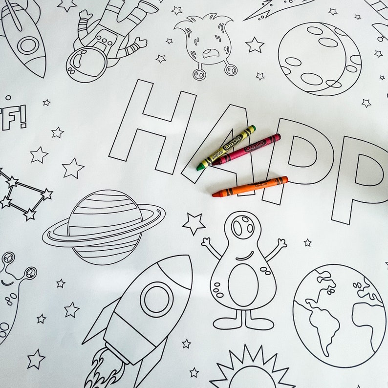 May include: A black and white coloring page with the word "HAPPY" written in large letters. The page features various space-themed illustrations, including a rocket, planets, stars, aliens, and an astronaut. Three crayons are placed on the page.