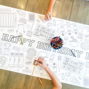 Può includere: Una tovaglia bianca a tema calcistico, con un grande striscione "HAPPY BIRTHDAY" e varie illustrazioni legate al calcio. La tovaglia è progettata per essere colorata con matite colorate o pennarelli.