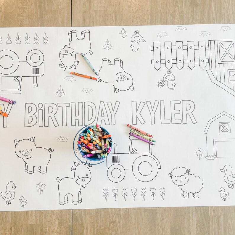 May include: A white colouring table cloth with a farm theme. The tablecloth features a tractor, a barn, a pig, a goat, a sheep, and a chicken. The text "Happy Birthday Kyler" is written on the tablecloth. There are crayons in a blue bowl on the tablecloth.