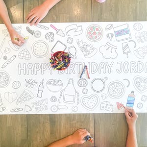 A large white paper tablecloth with a black outline design of pizza-themed illustrations and the text "HAPPY BIRTHDAY JORDAN". A red bowl of crayons and hands coloring the design are visible.