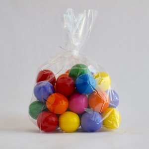 May include: A clear plastic bag filled with colorful gumballs. The gumballs are red, orange, yellow, green, blue, and purple.