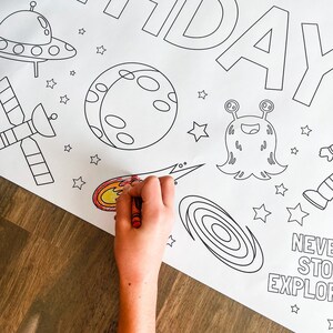May include: A black and white coloring page with a space theme. The page features a rocket, a satellite, a planet, a comet, a galaxy, a UFO, an alien, and stars. The text "Never Stop Exploring" is at the bottom of the page.