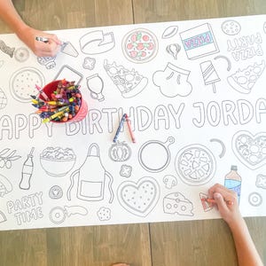 A large white paper coloring sheet with pizza-themed illustrations and the text "HAPPY BIRTHDAY JORDAN". A red bucket of crayons and two people coloring the sheet are visible.