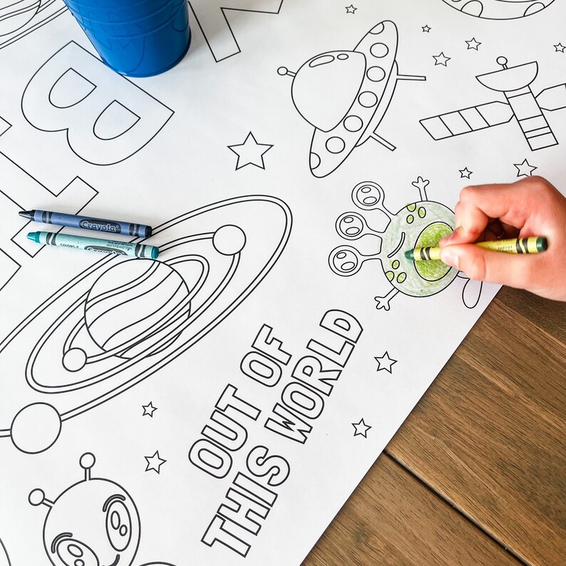 May include: A black and white coloring page with the text "Out of this world". The page features a spaceship, a planet, a satellite, and an alien. Crayola crayons are on the page.