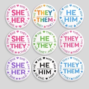 Puede incluir: Un conjunto de nueve chapas circulares con diversos pronombres de género. Cada chapa muestra una combinación de pronombres en el centro, rodeada por las mismas palabras repetidas en un borde circular, decoradas con corazones en colores a juego.