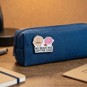 May include: A navy blue rectangular pencil case featuring an enamel pin attached to the front. The pin depicts a human head with a loading icon and a pink brain character carrying a briefcase, with the text MY BRAIN HAS LEFT THE CHAT.