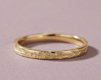 May include: A gold-toned metal ring featuring a continuous engraved pattern of small leaves and delicate floral motifs around the entire outer band. The ring has a smooth, polished finish and a slim, uniform width throughout its circular design.