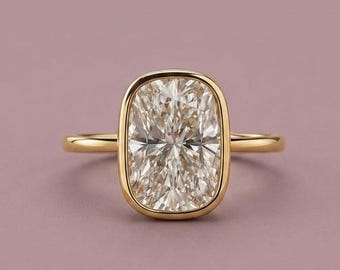 May include: A gold ring featuring a large, rectangular, cushion-cut clear gemstone set in a smooth, polished gold bezel setting. The band is thin and circular, crafted from the same yellow gold metal as the setting, creating a cohesive design.