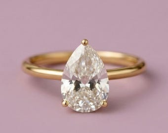 May include: A gold ring featuring a single pear-shaped faceted gemstone set in a four-prong mounting. The band is smooth and polished, showcasing a classic design with a clear, brilliant stone that tapers to a point at the top of the setting.