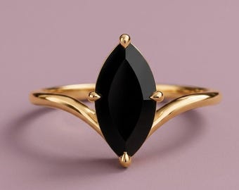 May include: A gold ring featuring a central marquise-cut black gemstone held by four prongs. The band has a smooth, polished finish and splits into two delicate arms that meet at the base of the stone setting, creating a V-shaped silhouette.