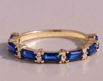 May include: A gold band ring featuring a series of alternating rectangular baguette-cut blue sapphires and small round clear stones set in a repeating pattern around the circumference of the metal band, creating a continuous decorative design.