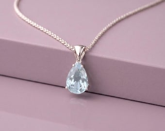 May include: A silver necklace featuring a pear-shaped, light blue gemstone pendant. The faceted stone is set in a polished silver metal frame and hangs from a delicate silver chain, creating a clear and reflective appearance in the light.