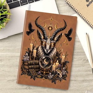 Puede incluir: Un cuaderno marrón con una ilustración detallada de una criatura con cuernos y ojos brillantes, rodeada de velas, cristales, libros apilados, una bola de cristal con una luna creciente y dos pájaros negros sobre un fondo celestial.