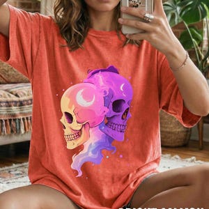May include: Bright salmon-colored t-shirt featuring a graphic of two stylized skulls. One skull is yellow and pink, the other is purple. The shirt has short sleeves and a relaxed fit. The text "BRIGHT SALMON" is printed at the bottom.
