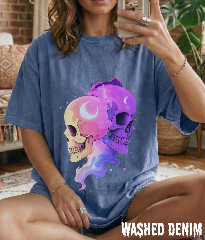 May include: A blue, short-sleeved t-shirt with a graphic of two skulls. One skull is pink and yellow, the other is purple. The graphic includes a crescent moon and a vaporous design. The words "WASHED DENIM" are printed at the bottom.