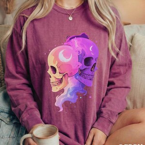 May include: Berry-colored sweatshirt featuring a graphic of two stylized skulls with crescent moon details. One skull is yellow and pink, the other is purple. The word "BERRY" is printed at the bottom right.