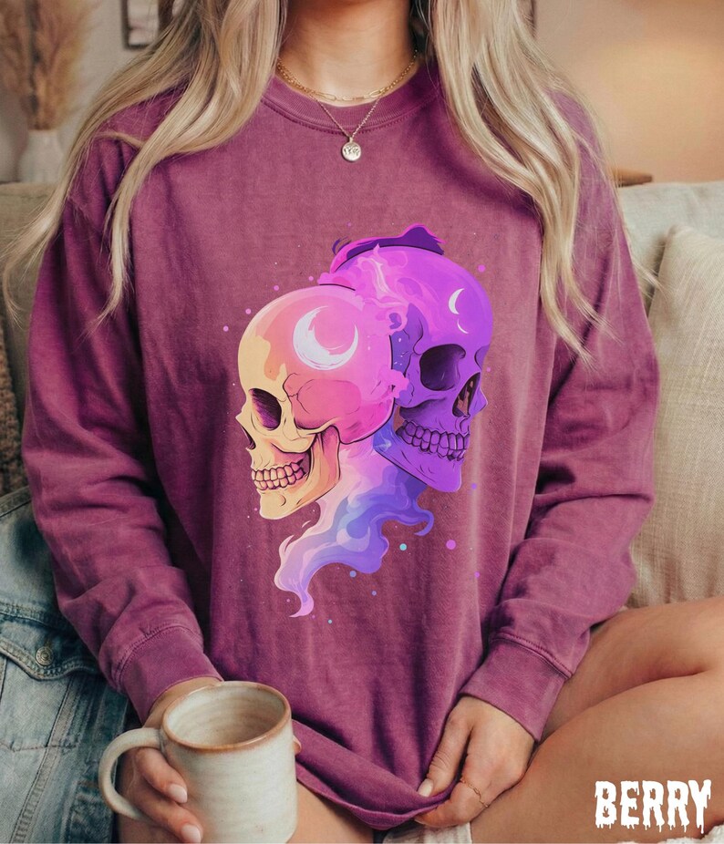 May include: Berry-colored sweatshirt featuring a graphic of two stylized skulls with crescent moon details. One skull is yellow and pink, the other is purple. The word "BERRY" is printed at the bottom right.