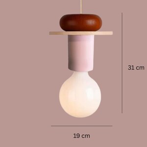 May include: A modern pendant light fixture with a large, round, white bulb. The fixture has a light pink cylindrical body, a wooden accent, and a dark brown wooden top. The overall height is 12.2 inches, and the bulb is 7.5 inches wide.