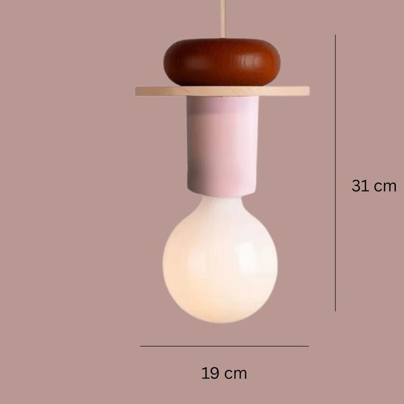 May include: A modern pendant light fixture with a large, round, white bulb. The fixture has a light pink cylindrical body, a wooden accent, and a dark brown wooden top. The overall height is 12.2 inches, and the bulb is 7.5 inches wide.