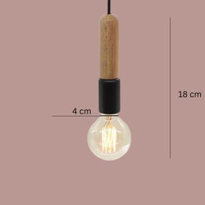Peut inclure: Un luminaire suspendu avec une section sup&eacute;rieure en bois, une section centrale noire et une ampoule transparente. L'ampoule mesure 4 cm de diam&egrave;tre et le luminaire mesure 18 cm de long. La lumi&egrave;re est suspendue &agrave; un cordon noir.