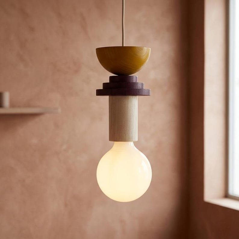 May include: A modern pendant light fixture with a warm, inviting glow. The design features a large, round light bulb at the bottom, topped with a wooden structure in shades of yellow, purple, and natural wood. The fixture hangs from a thin cord.