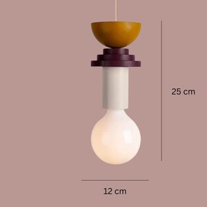 May include: A modern pendant light fixture with a unique design. The light features a wooden top in a yellow-brown hue, a dark purple midsection, a white cylindrical body, and a large, round, white light bulb. The fixture is approximately 9.8 inches tall and 4.7 inches wide.