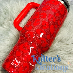 May include: A red glitter tumbler with a leopard print design and a red handle. The tumbler has a black lid and a white logo. The text "Kitter's Kreations" is visible on the side.