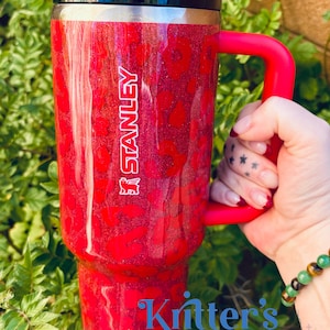 May include: Red Stanley tumbler with a leopard print design and a red handle. The tumbler has the Stanley logo in white. The text "Kritter's Kreations" is visible at the bottom of the tumbler.